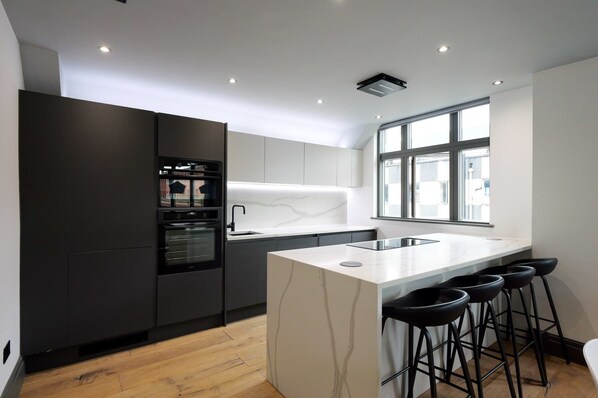 A modern kitchen with a central island, bar stools, and a large window providing natural light.