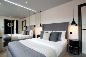 A modern hotel room with a large bed, bedside tables, a mirror, and a round light fixture.