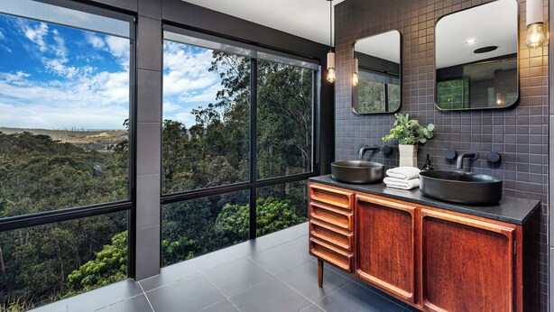 A modern bathroom with a large window, a wooden vanity, and a black sink.