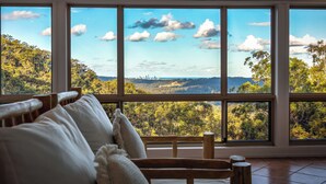 A room with large windows offering a view of a forested landscape and a distant city skyline.