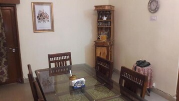 Uma área de refeições com mesa de vidro, cadeiras de madeira, um armário com portas de vidro e um quadro na parede.