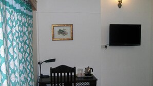 Una habitación con una mesa de madera, una silla, un cuadro enmarcado, un televisor montado en la pared y una lámpara de pared.