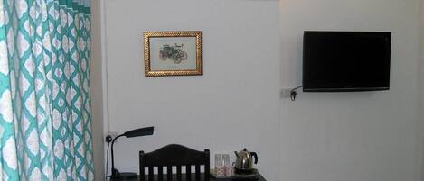 A room with a wooden table, a chair, a framed picture, a wall-mounted TV, and a wall sconce.