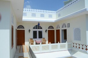 Um pátio com varanda branca, portas de madeira e painéis decorativos na parede.
