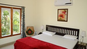 Habitación de hotel con cama, ventana con cortinas, aire acondicionado, lámpara de pared e imagen en un marco.