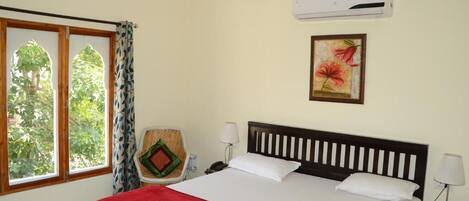 Habitación de hotel con cama, ventana con cortinas, aire acondicionado, lámpara de pared e imagen en un marco.