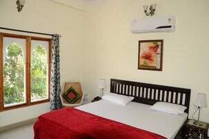 Quarto de hotel com cama, janela com cortinas, aparelho de ar condicionado, luminária fixada na parede e quadro emoldurado.