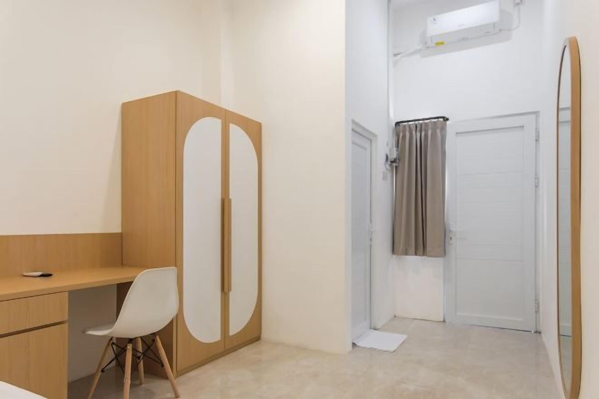 Une petite pièce propre, avec un bureau en bois, une chaise blanche, une armoire et une porte donnant sur une salle de bain.