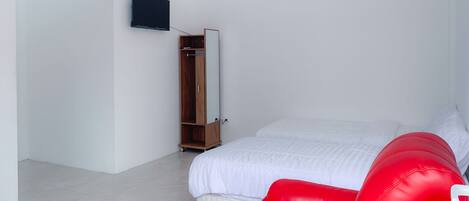 A bedroom with a bed, a red chair, a wardrobe, and a TV on the wall.