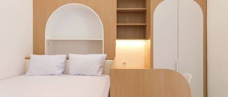 A bedroom with a bed, two white pillows, a bedside table, a nightstand, and a built-in shelf with a lamp.