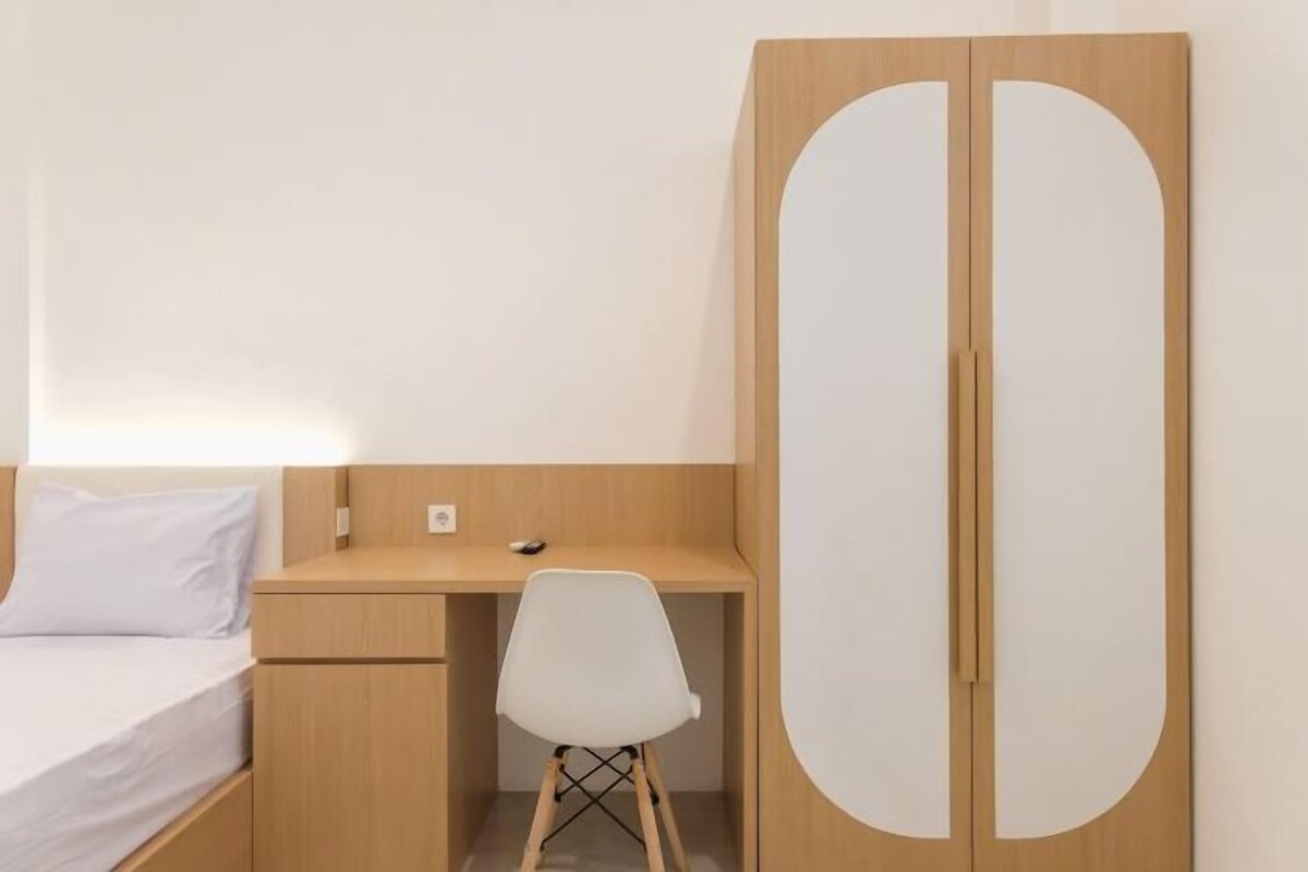 A bedroom with a bed, a desk, and a chair. There is a wardrobe with two doors.