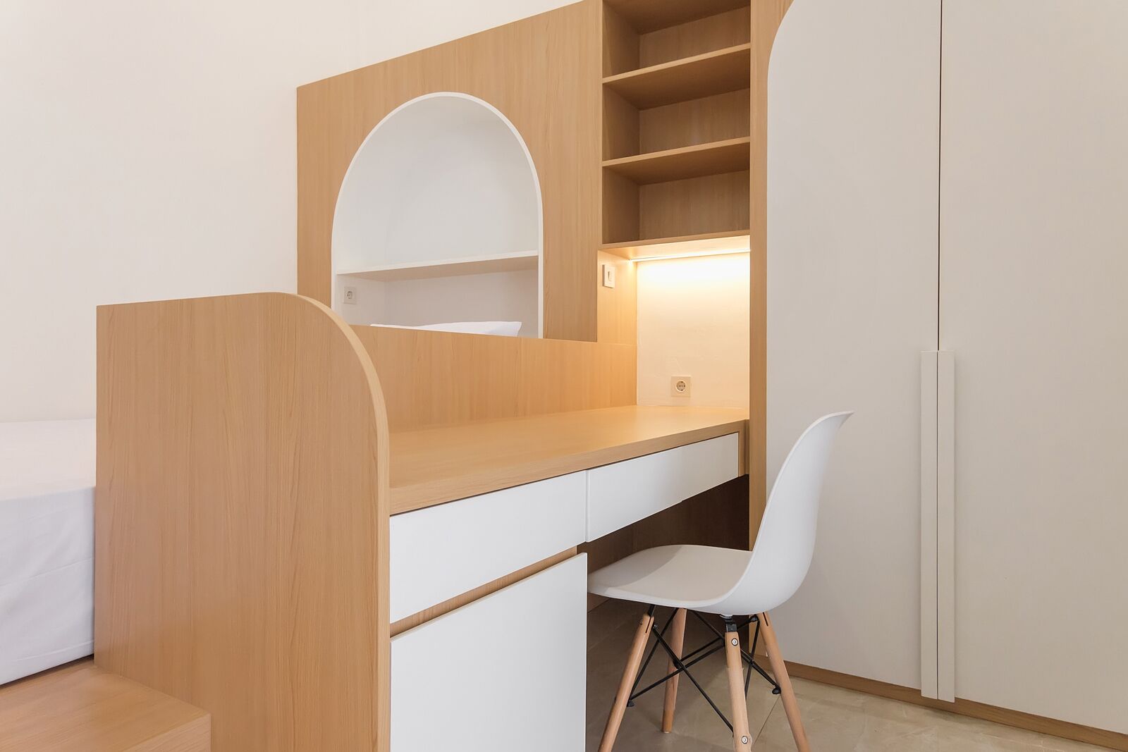 A modern bedroom with a wooden desk, white chair, and built-in shelving.