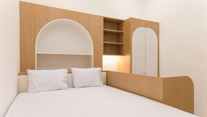 A bedroom with a bed, two white pillows, a wooden headboard, a built-in shelf, and a mirror. - Ipnoss Coliving Semarang, by INNCA COLLECTION (Semarang)