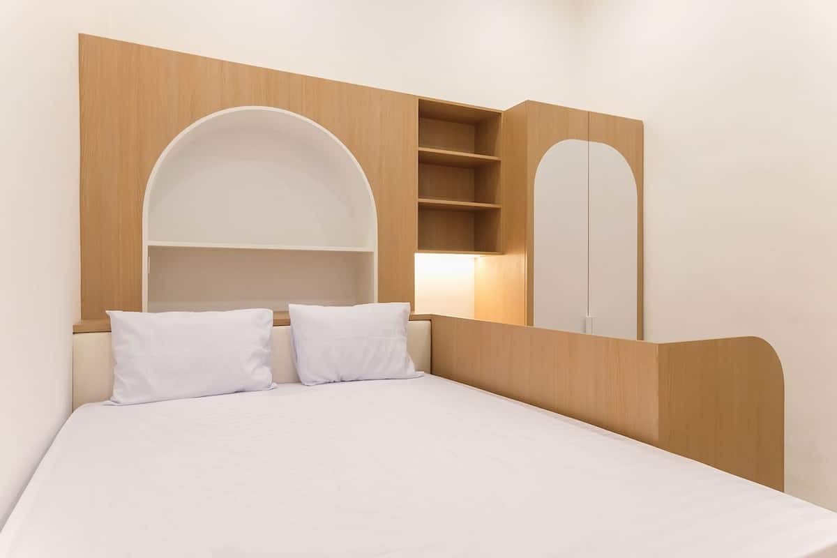 A bedroom with a bed, two white pillows, a wooden headboard, a built-in shelf, and a mirror.
