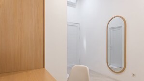 A small, clean room with a wooden floor, a white chair, a large mirror, and a white door. - Ipnoss Coliving Semarang, by INNCA COLLECTION (Semarang)