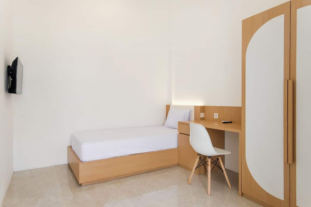 A minimalist bedroom with a single bed, a desk, and a chair.