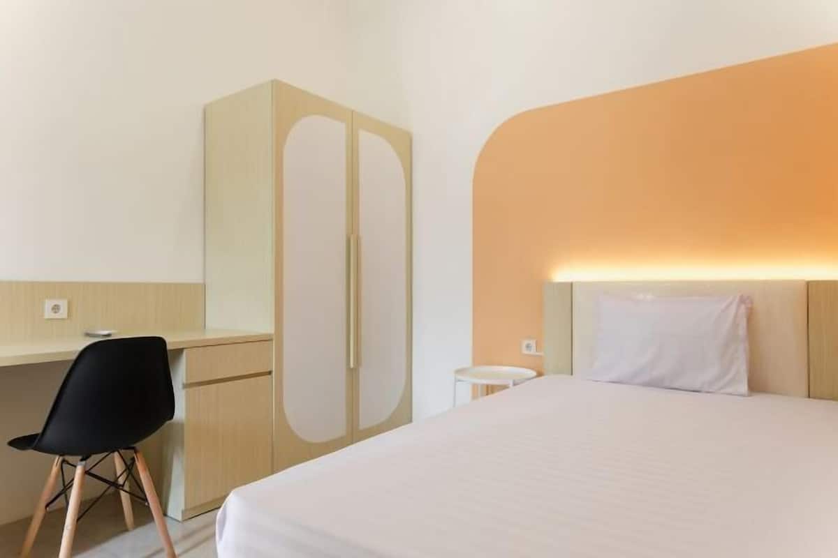 A hotel room with a bed, a desk, a chair, and a wardrobe.