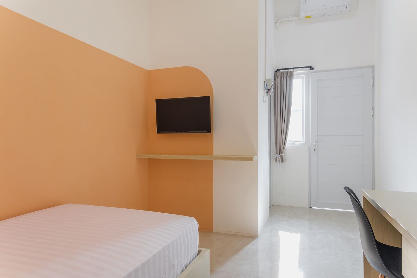 Een slaapkamer met een bed, een tv aan de muur, een bureau en een deur naar een badkamer.
