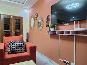 A living room with a sofa, a television mounted on the wall, decorative mirrors, and a small plant on a shelf. - Hidden Gem in Ouakam [Mamelles] (Dakar)