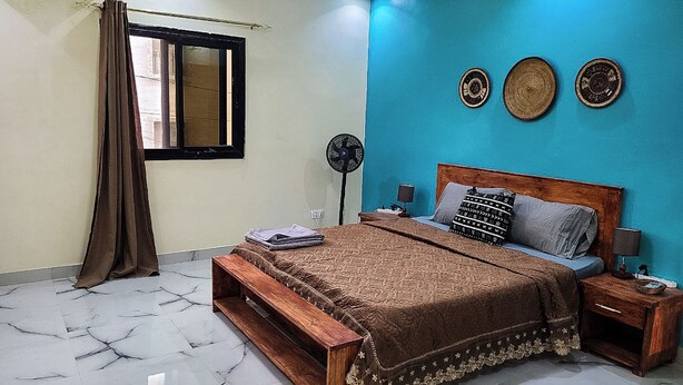 A bedroom with a bed, a bedside table, a nightstand, a fan, and a window with curtains. - Hidden Gem in Ouakam [Mamelles] (Dakar)