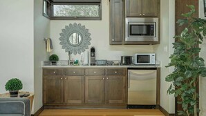 A kitchen with wooden cabinets, stainless steel appliances, a sunburst mirror, and a potted plant. - Relaxing Lake Escape | 1BR | Pickleball | BBQ (Lake Travis)
