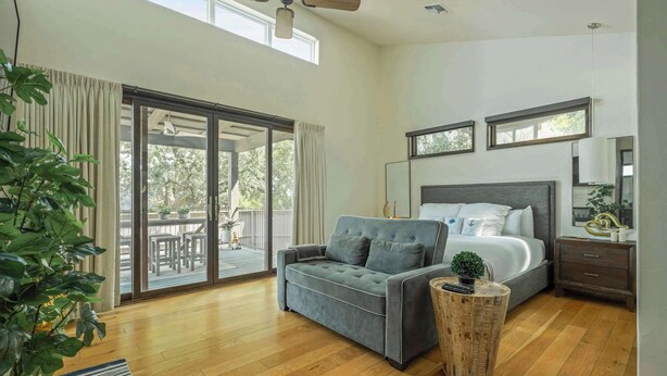 A bedroom with a bed, a sofa, a small table, and a sliding glass door leading to an outdoor area. - Relaxing Lake Escape | 1BR | Pickleball | BBQ (Lake Travis)