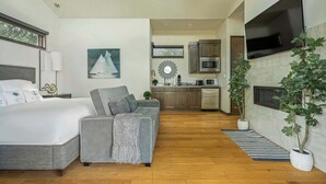 A modern hotel room with a bed, sofa, TV, kitchen area, and potted plants. - Relaxing Lake Escape | 1BR | Pickleball | BBQ (Lake Travis)