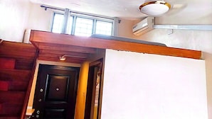 Una habitación con techo inclinado, ventana, equipo de aire acondicionado y puerta de madera.