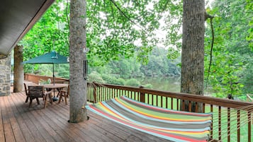A wooden deck with a hammock, a table, and chairs, overlooking a forested area.