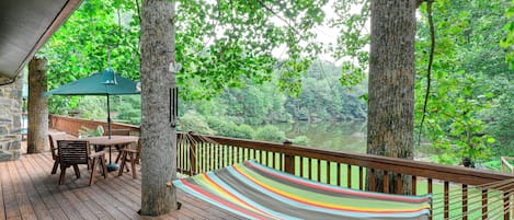 Eine Holzterrasse mit einer Hängematte, einem Tisch und Stühlen mit Blick auf ein bewaldetes Gebiet.
