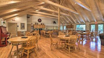 A spacious dining area with wooden tables and chairs, a piano, and a kitchen in the background.