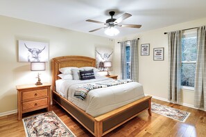 A bedroom with a wooden bed, a ceiling fan, and a large window with curtains. - Deck & Game Room! Lakefront Blue Ridge Mtn Gem (Deep Gap)