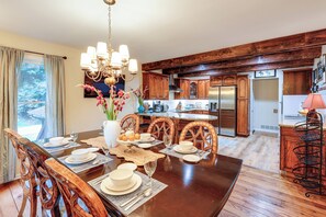 A dining room with a wooden table set for four, surrounded by wooden chairs. A chandelier hangs above, and a vase with flowers is on the table. - Deck & Game Room! Lakefront Blue Ridge Mtn Gem (Deep Gap)
