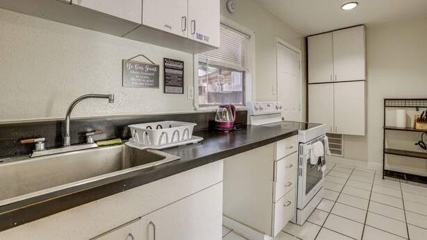 A kitchen with white cabinets, a stainless steel sink, a toaster, and a window with blinds. - Suburban Home By Arthur Storey Park & HCA Houston! (Houston)