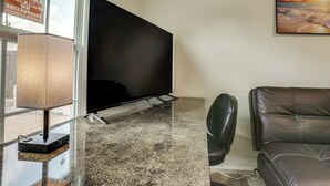 A modern living room with a flat-screen TV on a stand, a leather sofa, a coffee table, and a lamp. - Suburban Home By Arthur Storey Park & HCA Houston! (Houston)