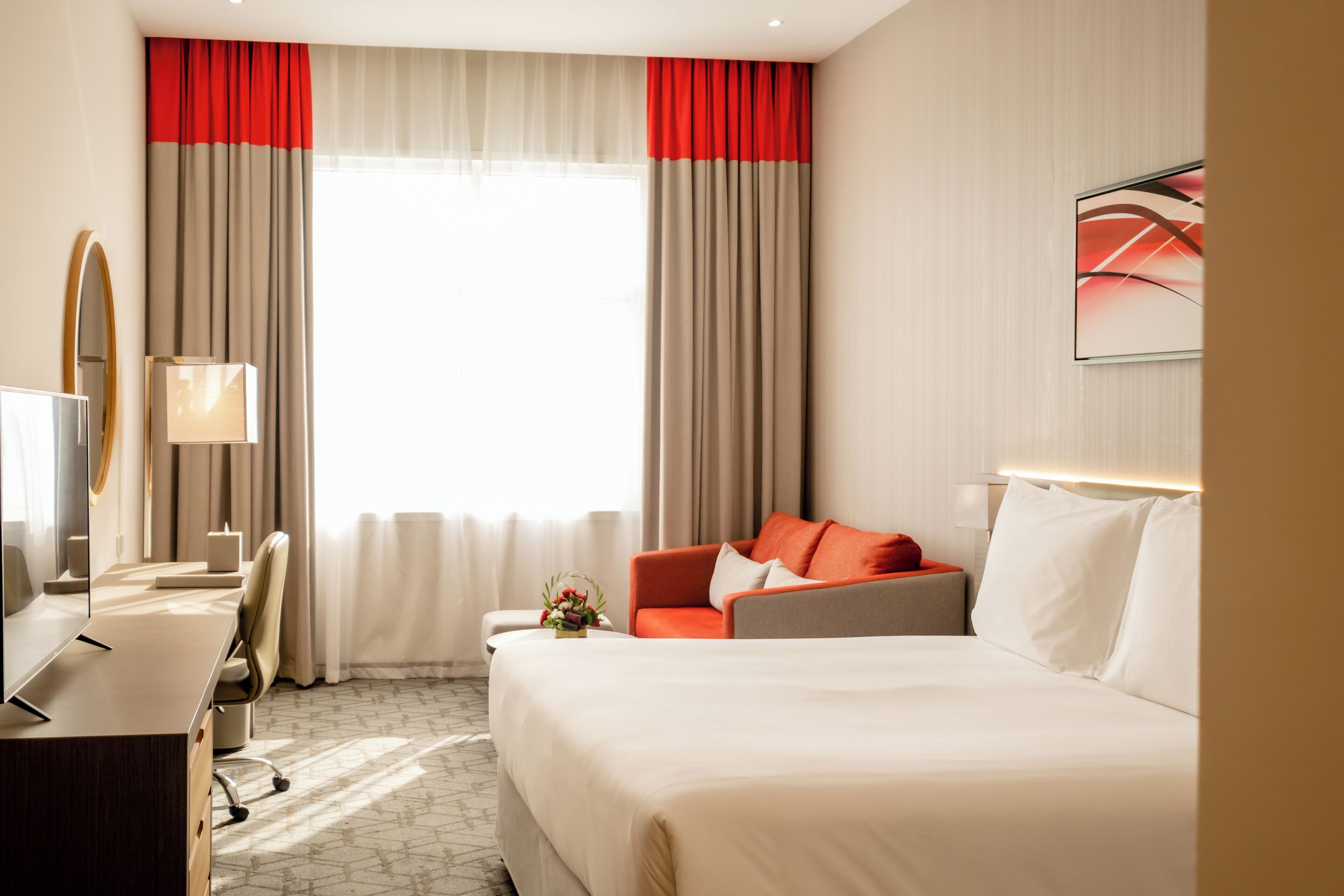 Hotelkamer met een bed, bureau, stoel, een bank en een groot raam met gordijnen.