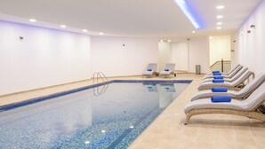 Una piscina con sillones de descanso y suelo de baldosas.