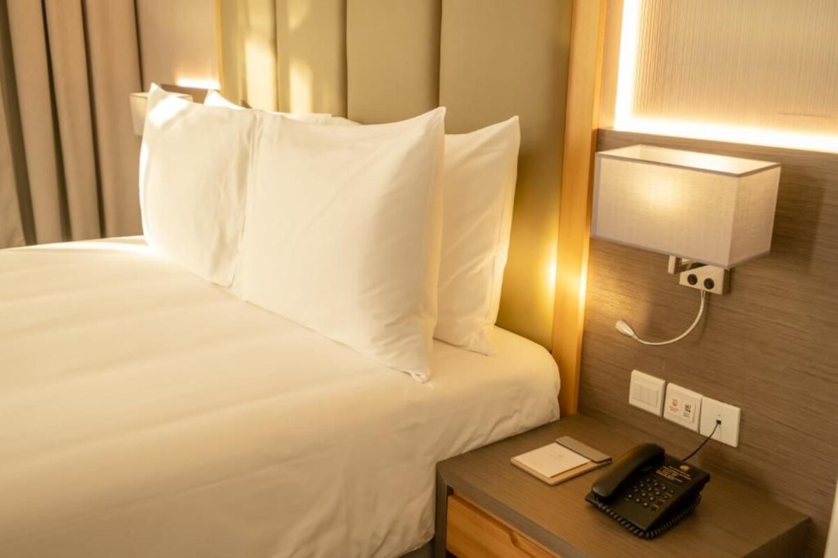A hotel room with a neatly made bed, a bedside table with a lamp, and a phone.