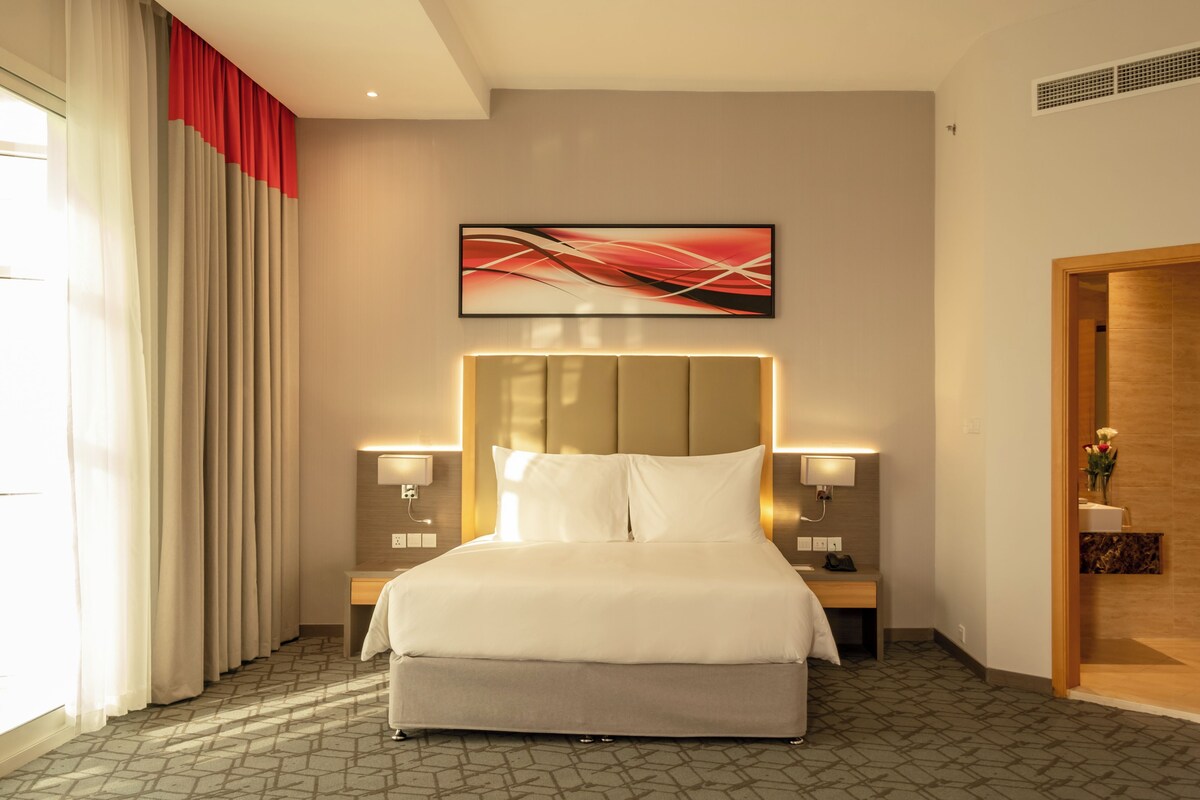 Habitación de hotel con una cama grande, dos mesitas de noche con lámparas, un cabecero y un cuadro en la pared.