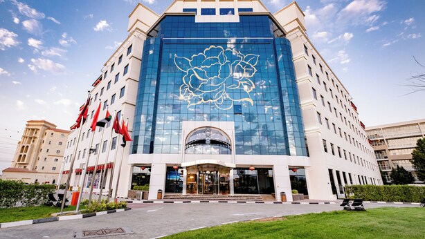 Un hotel moderno con una amplia fachada de vidrio, una entrada central y varias banderas.