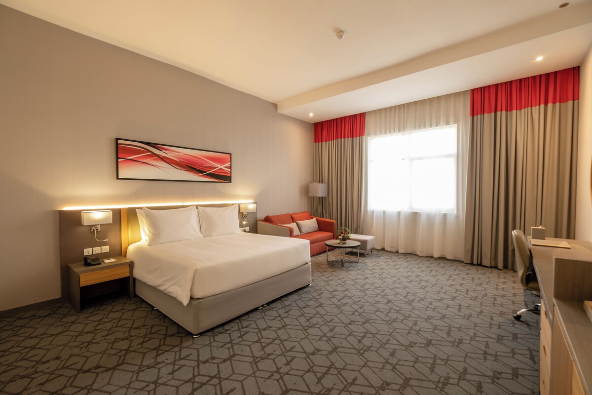 Habitación de hotel con una cama grande, un escritorio, una silla, un sofá y una ventana con cortinas.
