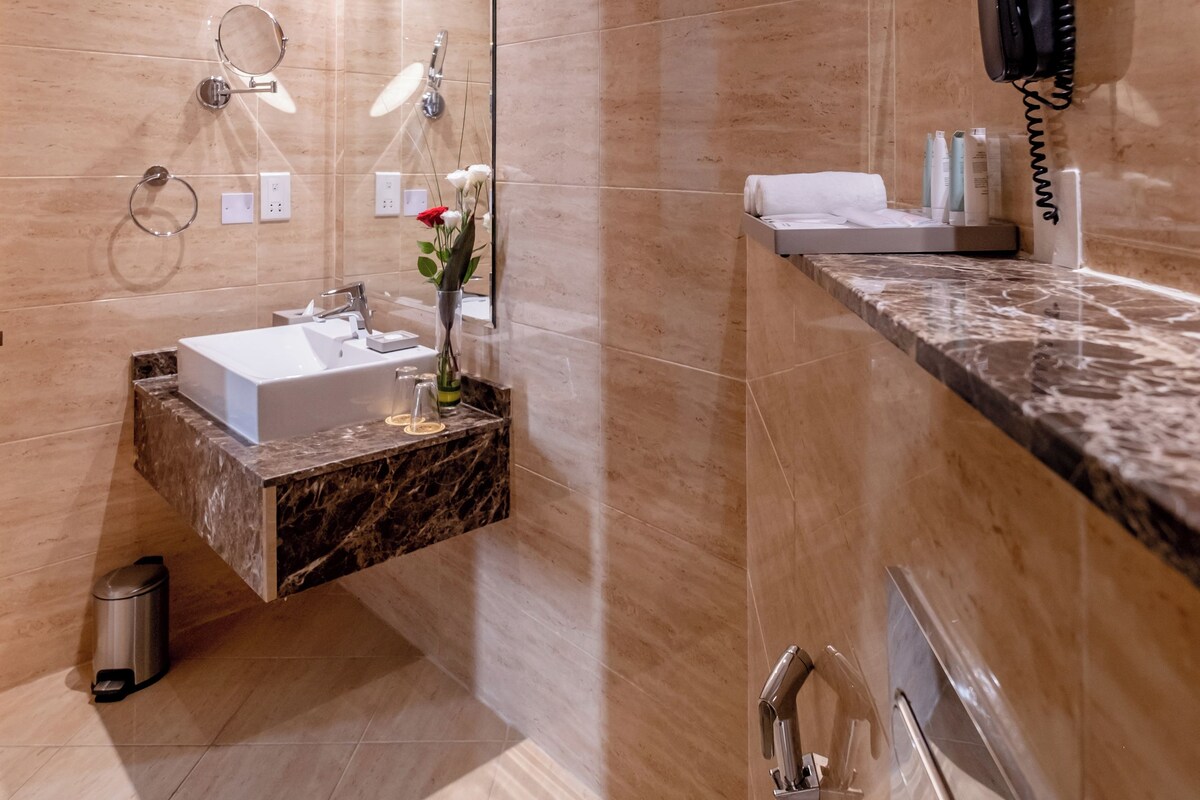 A modern bathroom with a marble sink, a handheld showerhead, and a mirror with a ring light.