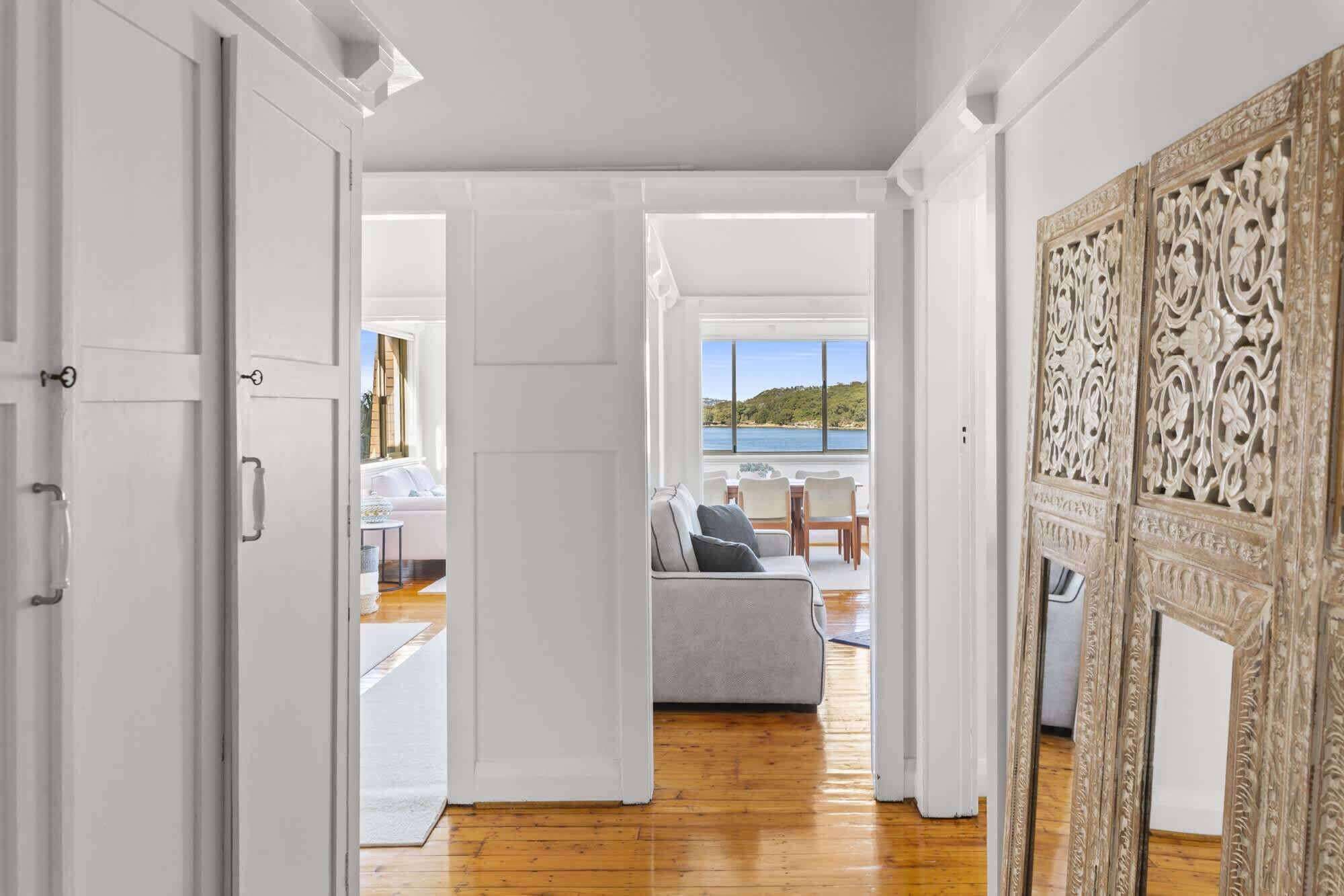 A spacious room with a wooden floor, a large window offering a view of the sea, and a white door leading to another area.