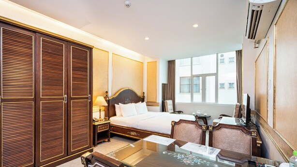 A hotel room with a large bed, a desk with a chair, a wardrobe, and a window with a view of buildings. - Nicecy Hotel & Apartment - Central Sai Gon (Ho Chi Minh City)