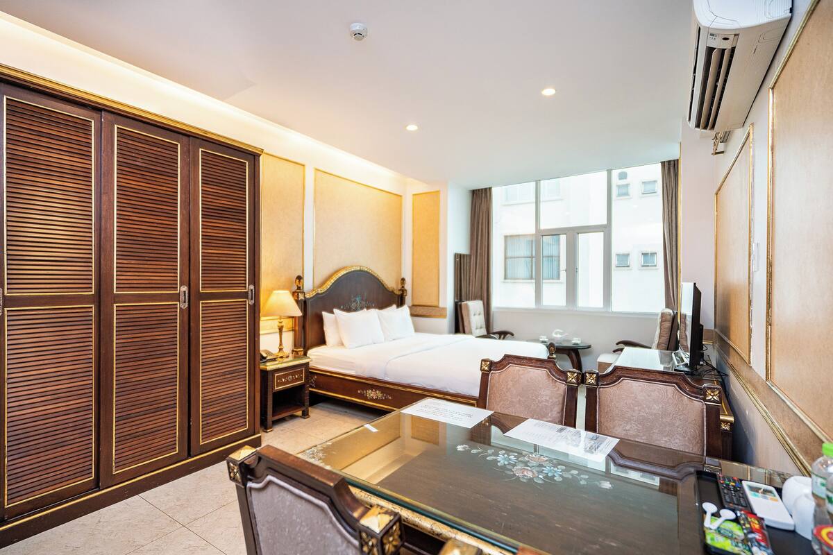 Ein Hotelzimmer mit einem großen Bett, einem Schreibtisch mit Stuhl, einem Kleiderschrank und einem Fenster mit Blick auf Gebäude.