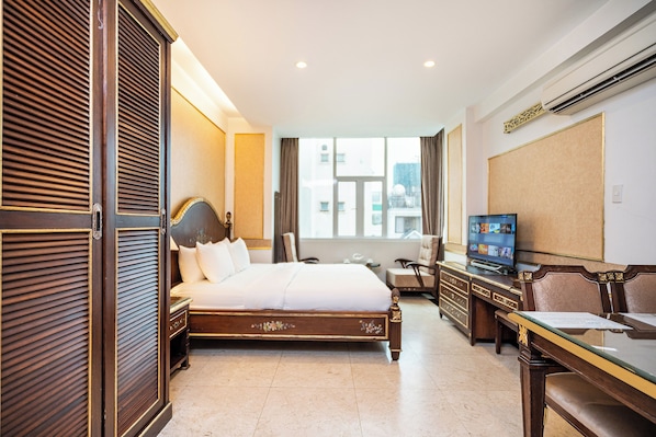 Quarto de hotel com uma cama grande, televisão, escrivaninha e vista para a cidade.