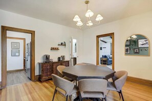 A dining area with a large table, four chairs, a chandelier, a cabinet, and a mirror on the wall.