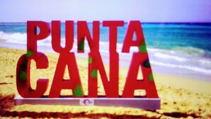 Una señal con la palabra 'PUNTA CANA' en una playa, con el océano al fondo.
