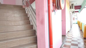 A staircase with wooden steps and metal railings, leading to a hallway with pink walls and a checkered floor. - Dhanas Residency Pondicherry (Puducherry)