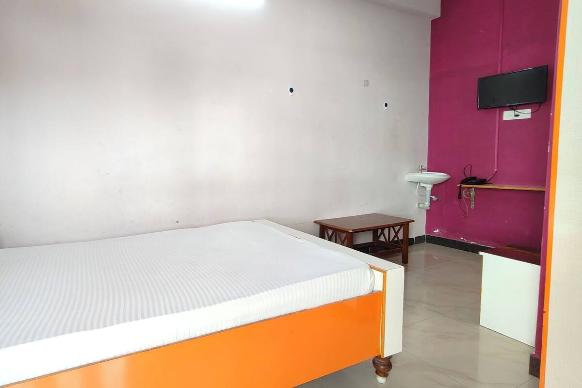 Quarto com uma cama, uma mesa pequena, uma pia e uma televisão.